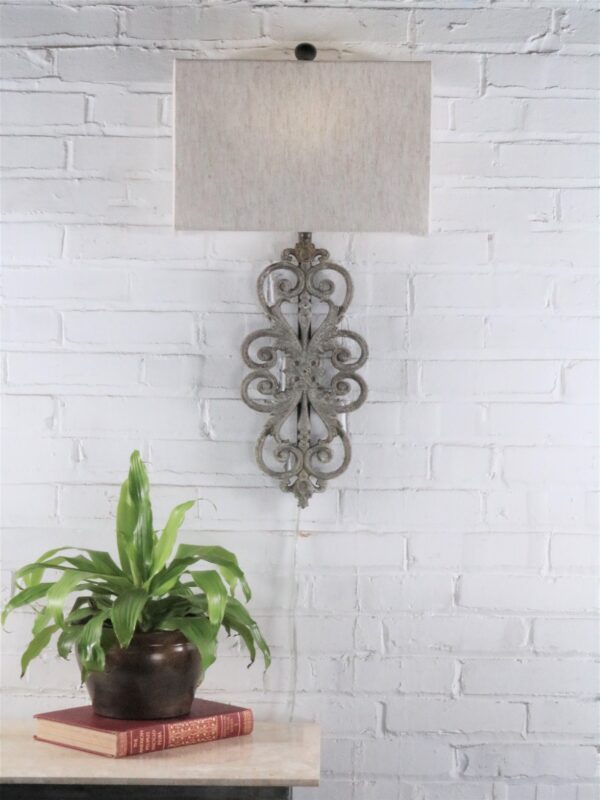 Scrollwork custom iron wall sconce with a gray, distressed finish. Paired with a half rectangle linen lamp shade.